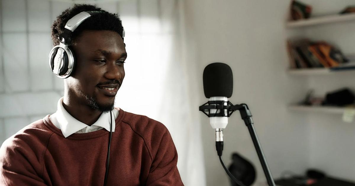 Man wearing headphones speaking into a microphone during an online recording session.