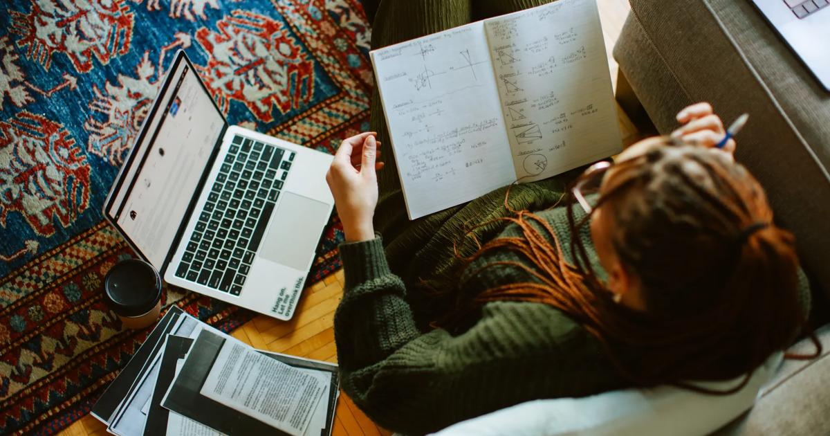 Overhead view of a college student studying at home with a laptop and books