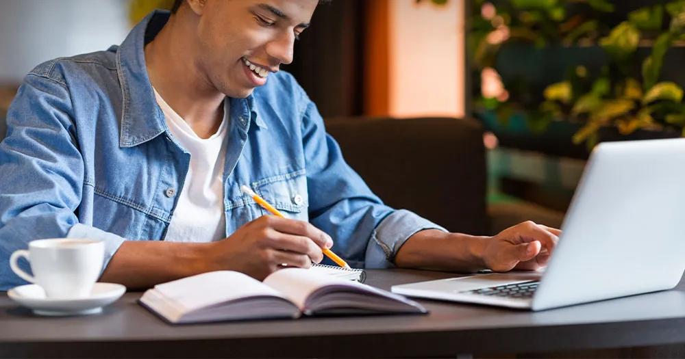 Student studying at a laptop, taking notes in a notebook.