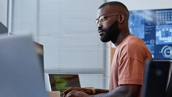 A data professional works at a desk with multiple computer monitors displaying different information.