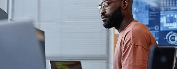 A data professional works at a desk with multiple computer monitors displaying different information.