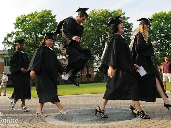 Graduates in caps and gowns walking across campus during commencement.