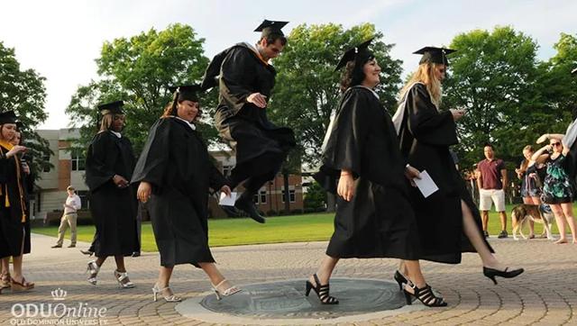 Graduates in caps and gowns walking across campus during commencement.