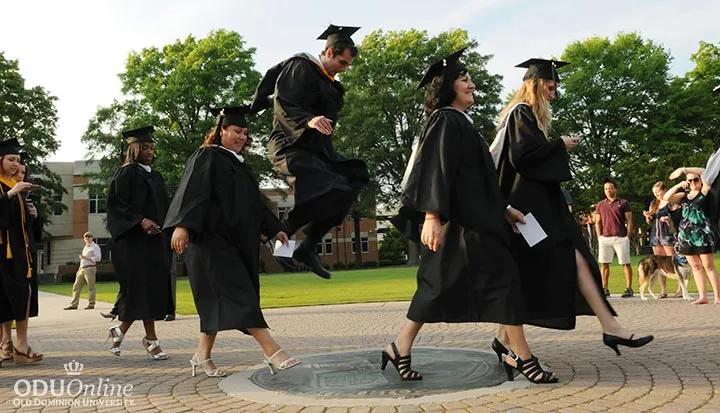 Graduates in caps and gowns walking across campus during commencement.