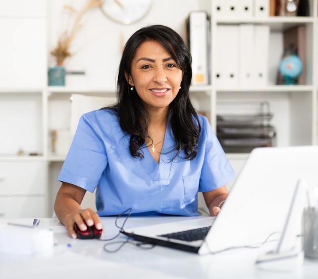 Portrait of female nurse in blue scrubs uniform working at computer