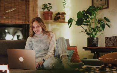 A young woman sitting comfortably on a couch using a laptop during a cozy and festive evening at home