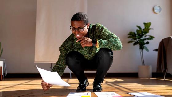 A man kneels as he organizes papers on the floor. 