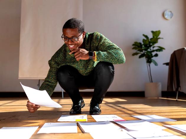 A man kneels as he organizes papers on the floor. 