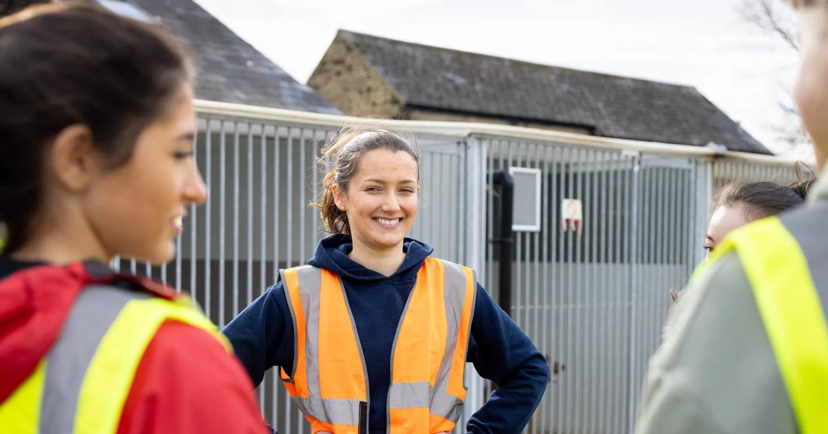 A woman wearing a safety vest smiles at her peers as they stand outside in a residential area.