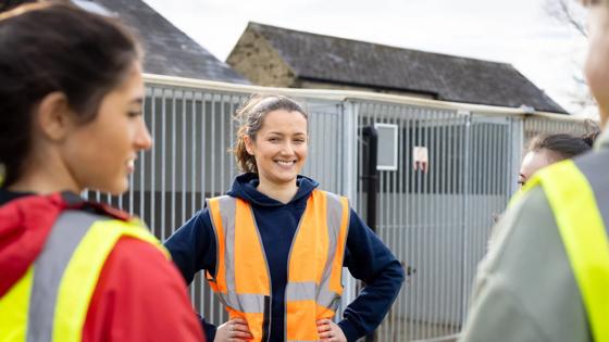 A woman wearing a safety vest smiles at her peers as they stand outside in a residential area.
