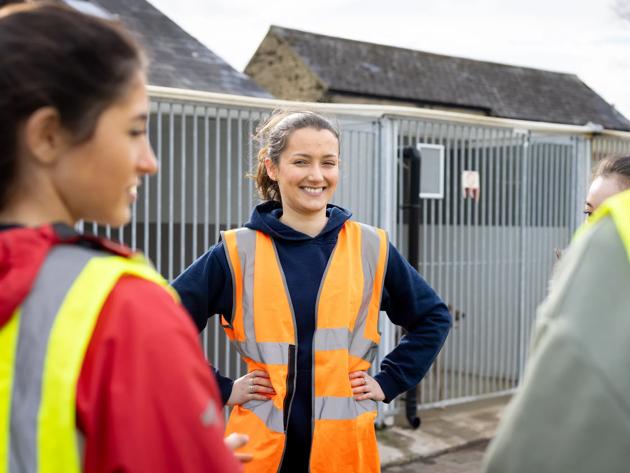A woman wearing a safety vest smiles at her peers as they stand outside in a residential area.