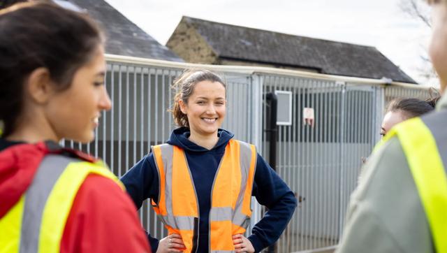 A woman wearing a safety vest smiles at her peers as they stand outside in a residential area.