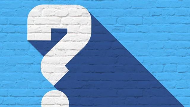 A white question mark painted on a blue brick wall.