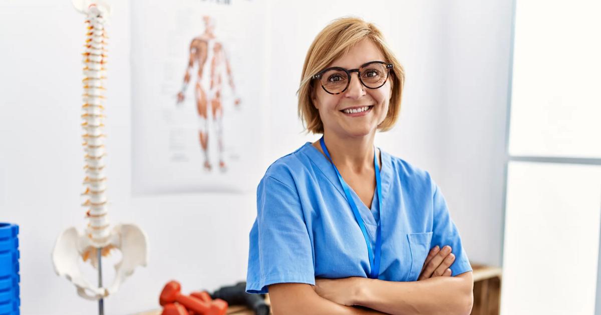 A kinesiology professional stands confidently in a clinical setting.