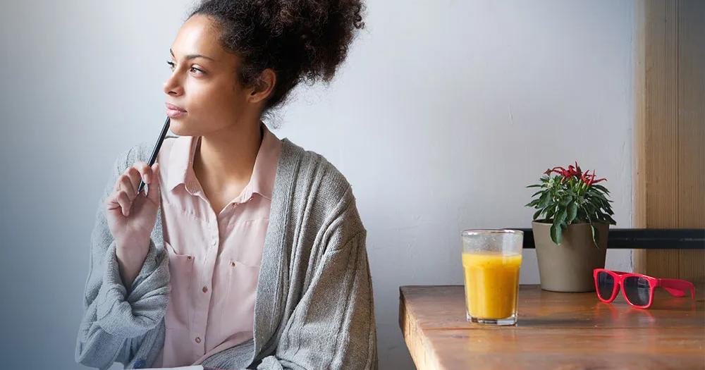 Woman holding a pen and notebook while sitting at a table.