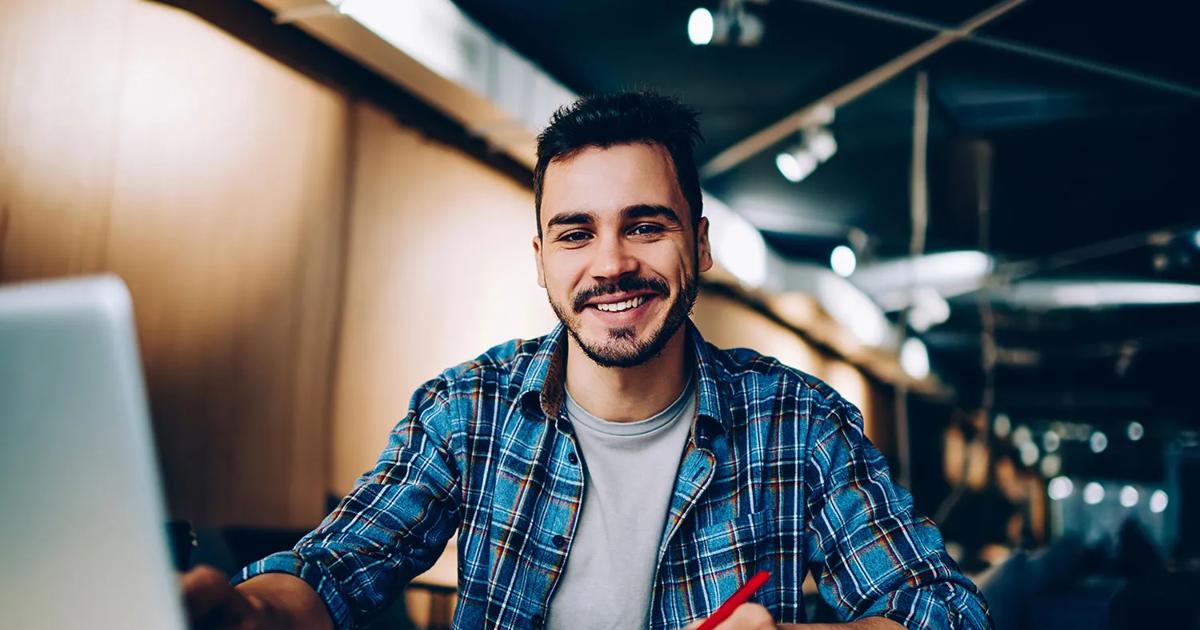 A cheerful male student works on a latop in the library.
