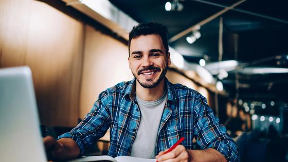 A cheerful male student works on a latop in the library.
