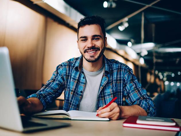 A cheerful male student works on a latop in the library.