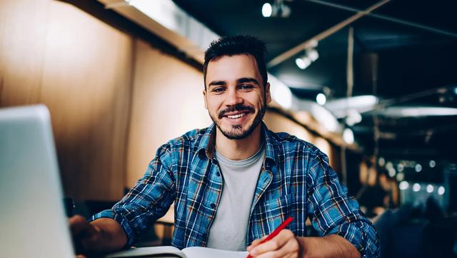 A cheerful male student works on a latop in the library.