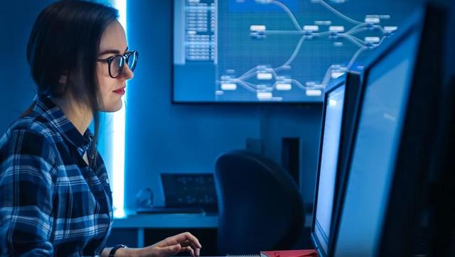 A female professional in the cybersecurity field works at a computer on a desk with dual monitors.
