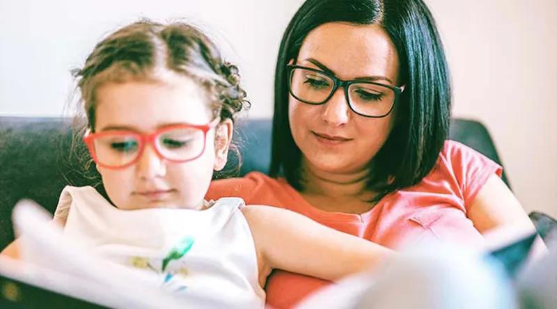 Mother and daughter wearing glasses reading together on a couch.