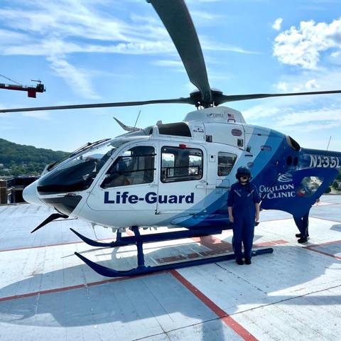 Baylee Slagle poses in front of a medical helicopter, wearing a flight suit and helmet.