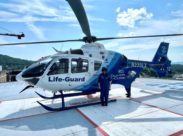 Baylee Slagle poses in front of a medical helicopter, wearing a flight suit and helmet.
