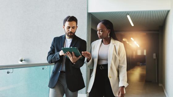 Business people walk with a digital tablet to discuss a meeting briefing.