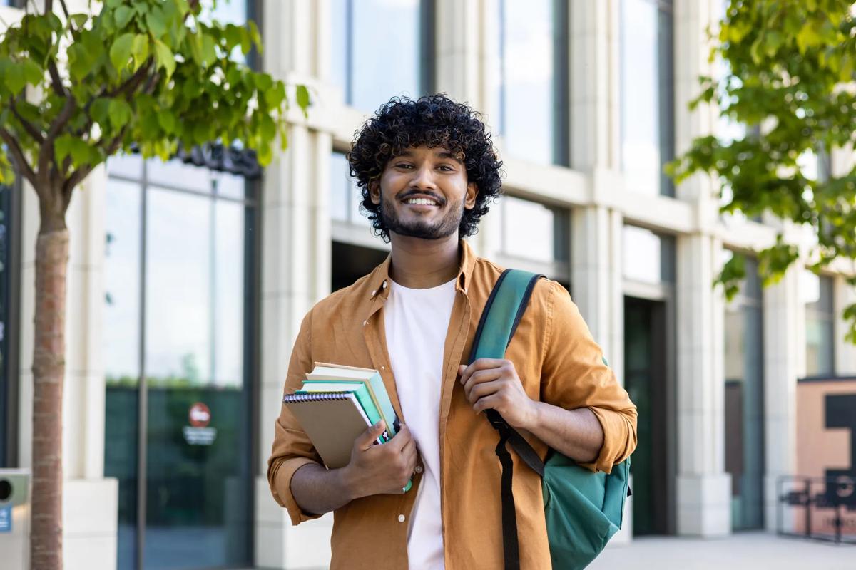 Portrait_of_Young_Smiling_Male_Indian_Student_outside_University_with_Books