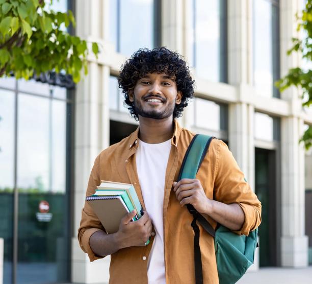 Portrait_of_Young_Smiling_Male_Indian_Student_outside_University_with_Books