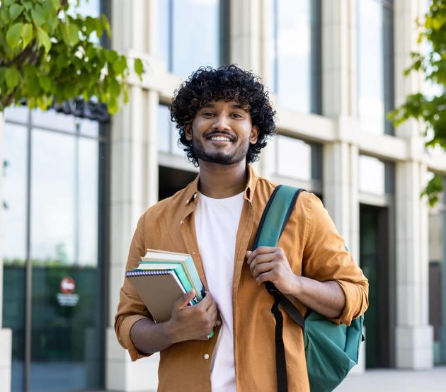 Portrait_of_Young_Smiling_Male_Indian_Student_outside_University_with_Books