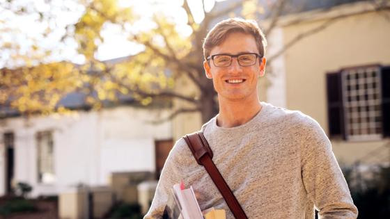 Happy male college student outdoors with books. Young university student with books in campus.