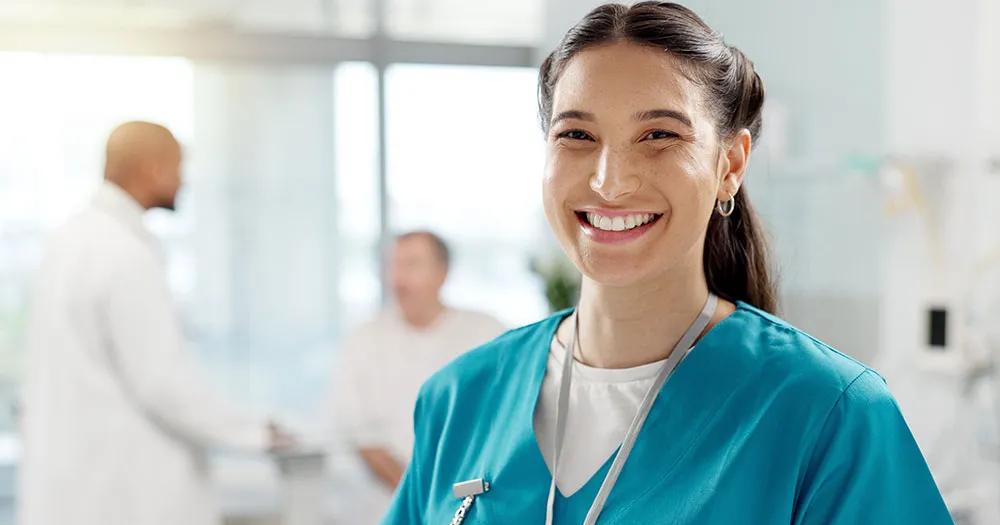 Nurse in scrubs holding a tablet in a clinical setting.