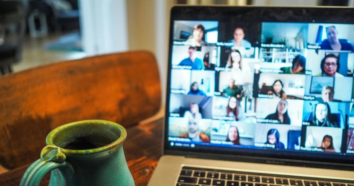 Laptop showing a virtual meeting beside a coffee mug on a desk.