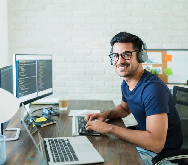 A cybersecurity professional looks up from typing at a desktop computer and smiles.