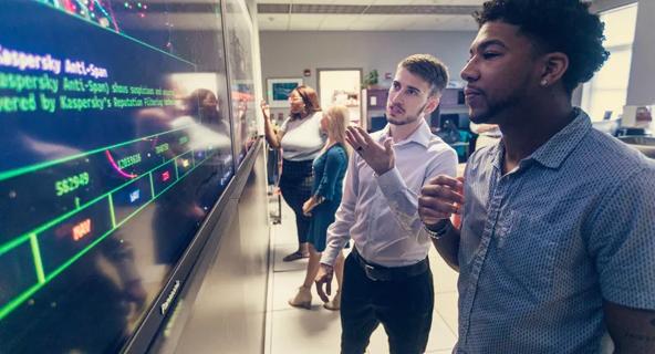 Computer professionals meet in front of a large display screen.