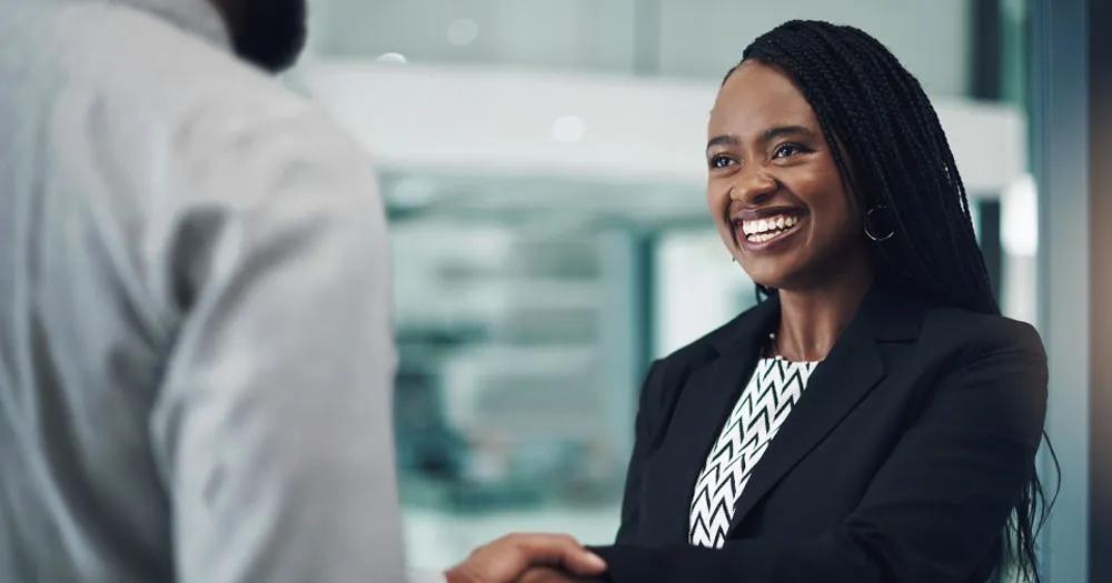 Professional women smiling while shaking hands in an office setting.