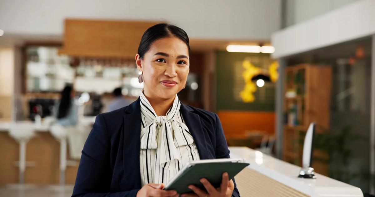 A hotel manager stands in a reception area holding a digital tablet for guest check in.