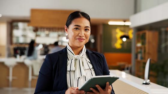 A hotel manager stands in a reception area holding a digital tablet for guest check in.