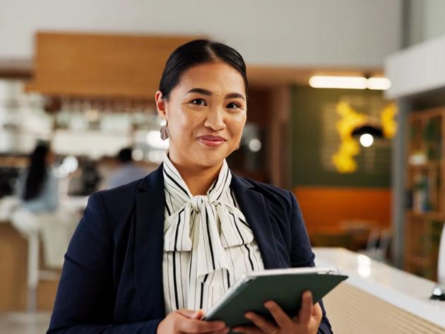 A hotel manager stands in a reception area holding a digital tablet for guest check in.