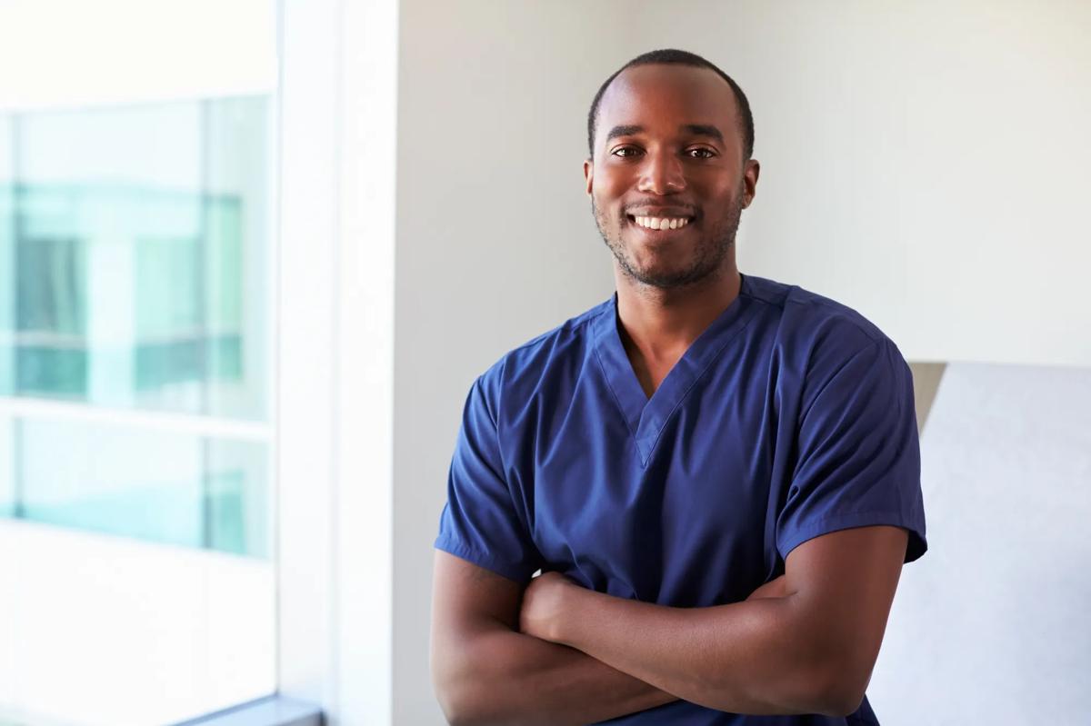 Man in blue scrubs smiling at the camera.