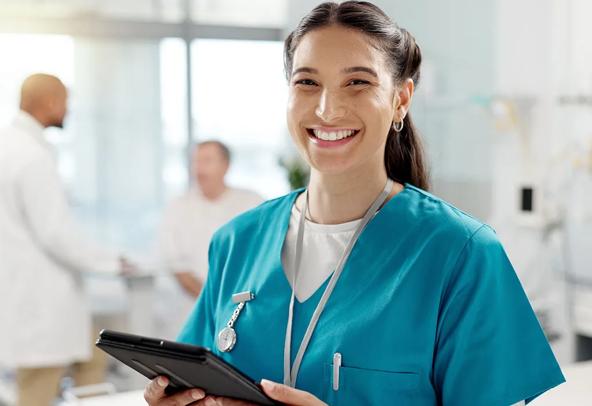 A confiden female nursing gradaute smiles at the camera while holding a tablet device.