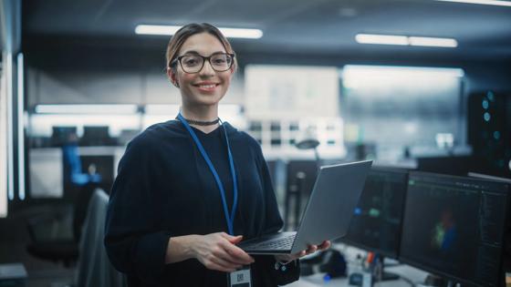 Woman stands holding a laptop in a workspace with servers.
