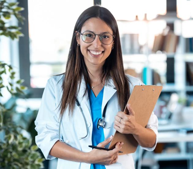 Medical and Health Professions Education (MHPE) faculty member smiling and holding a clipboard in the classroom.