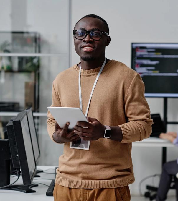 An IT specialist in eyeglasses smiles at camera while working online in an open office space