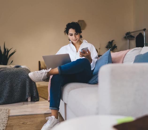 Content woman browsing smartphone and laptop on cozy sofa