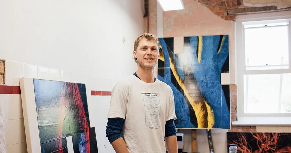Man standing in an art studio with paintings behind him.