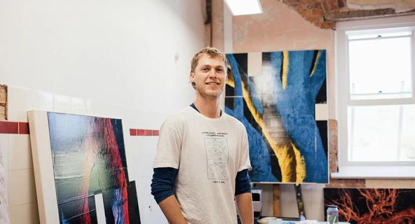Man standing in an art studio with paintings behind him.
