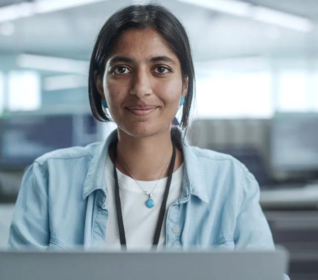 A confident woman looks up from her desk in a technology-centered office.
