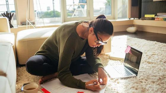 Woman sitting on floor with laptop and study notes